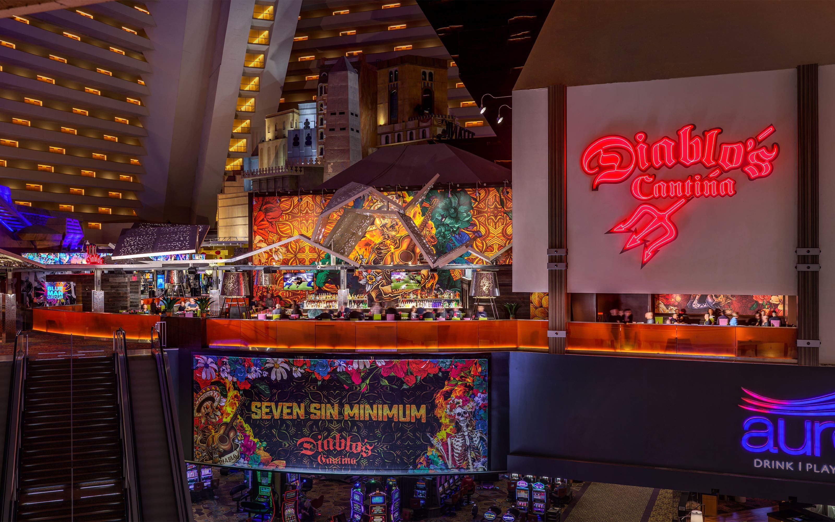 Zona de bar vibrante con letreros de neón, una gran pantalla digital que muestra 'Seven Sin Minimum' y un salón de casino con máquinas tragamonedas.
