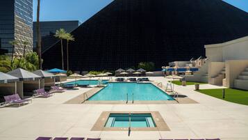 A pool area with lounge chairs and umbrellas, a no diving sign, and a large building in the background.