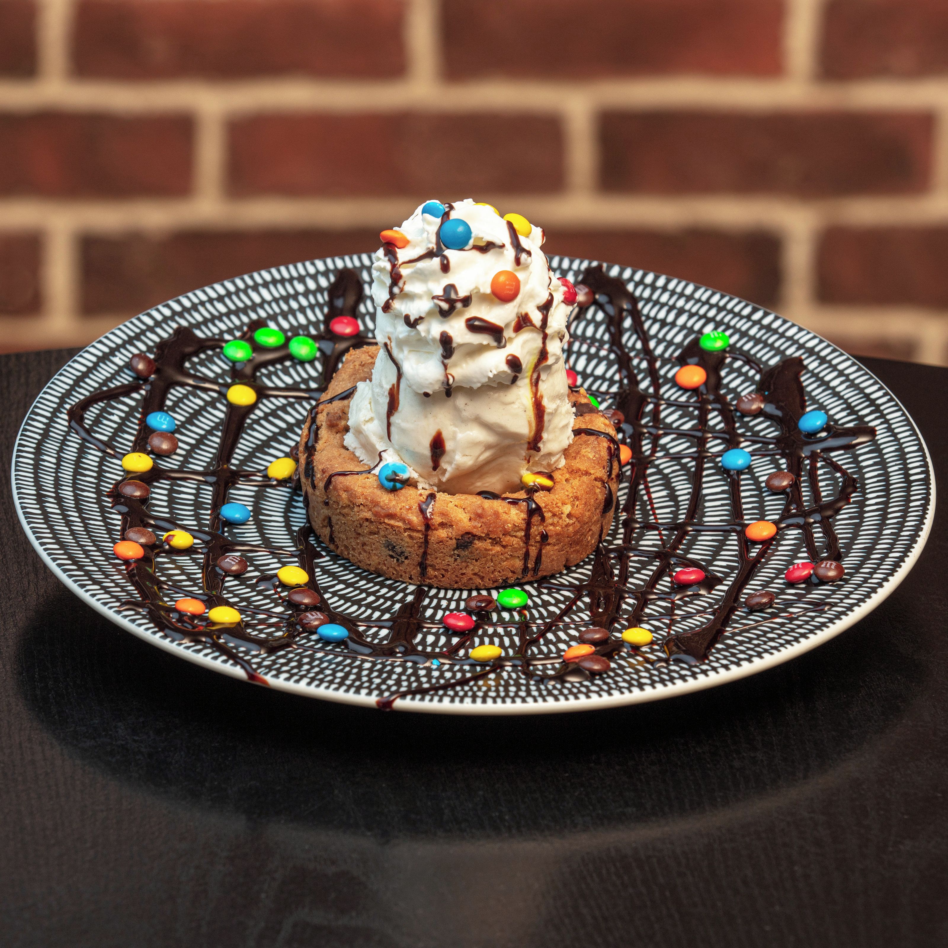 Un postre en un plato estampado, con caramelos de colores y un chorrito de chocolate.