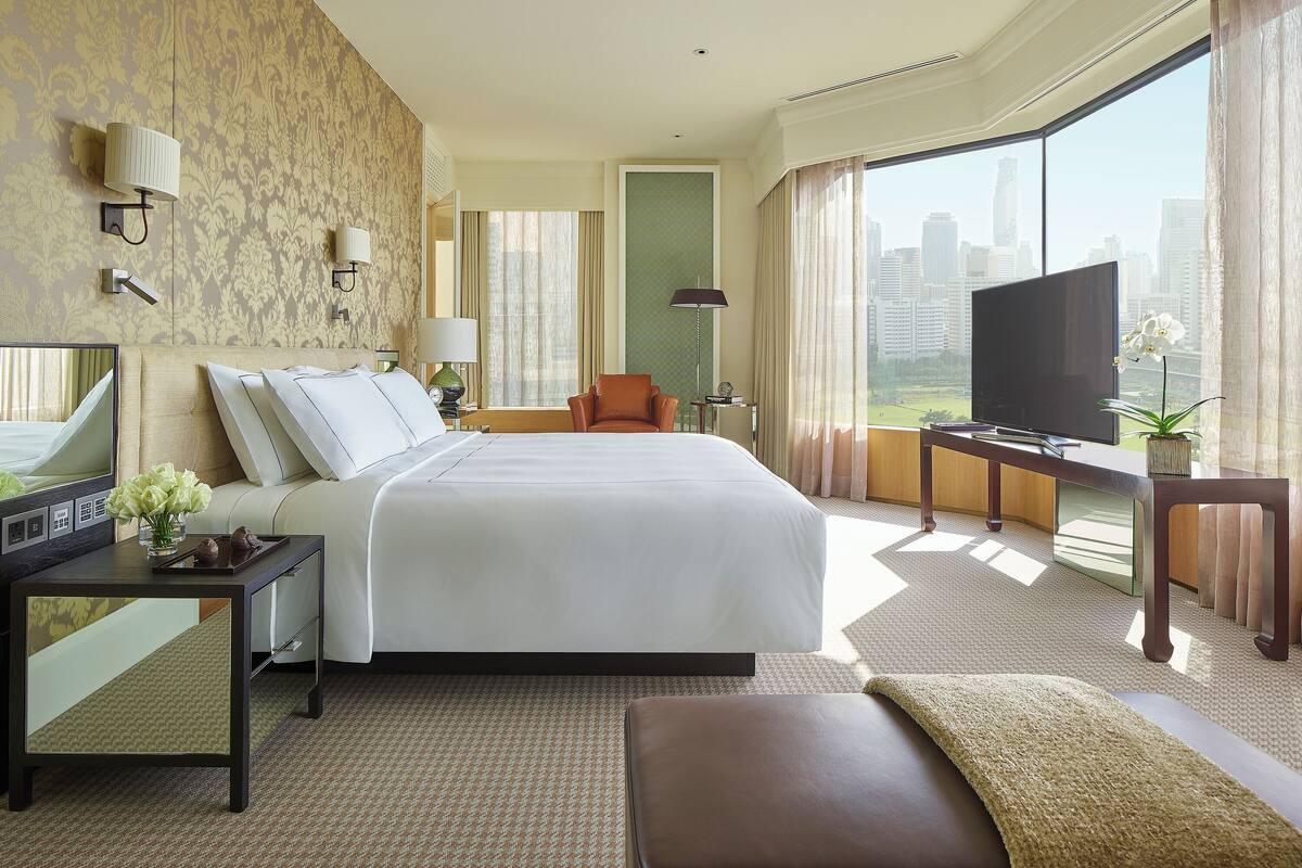 Habitación de hotel con una cama grande, televisión, escritorio con lámpara y vistas a la ciudad.