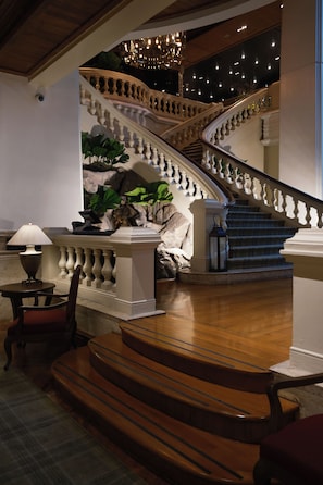 Een statige trap met een balustrade, een kroonluchter en een lamp op een tafel.