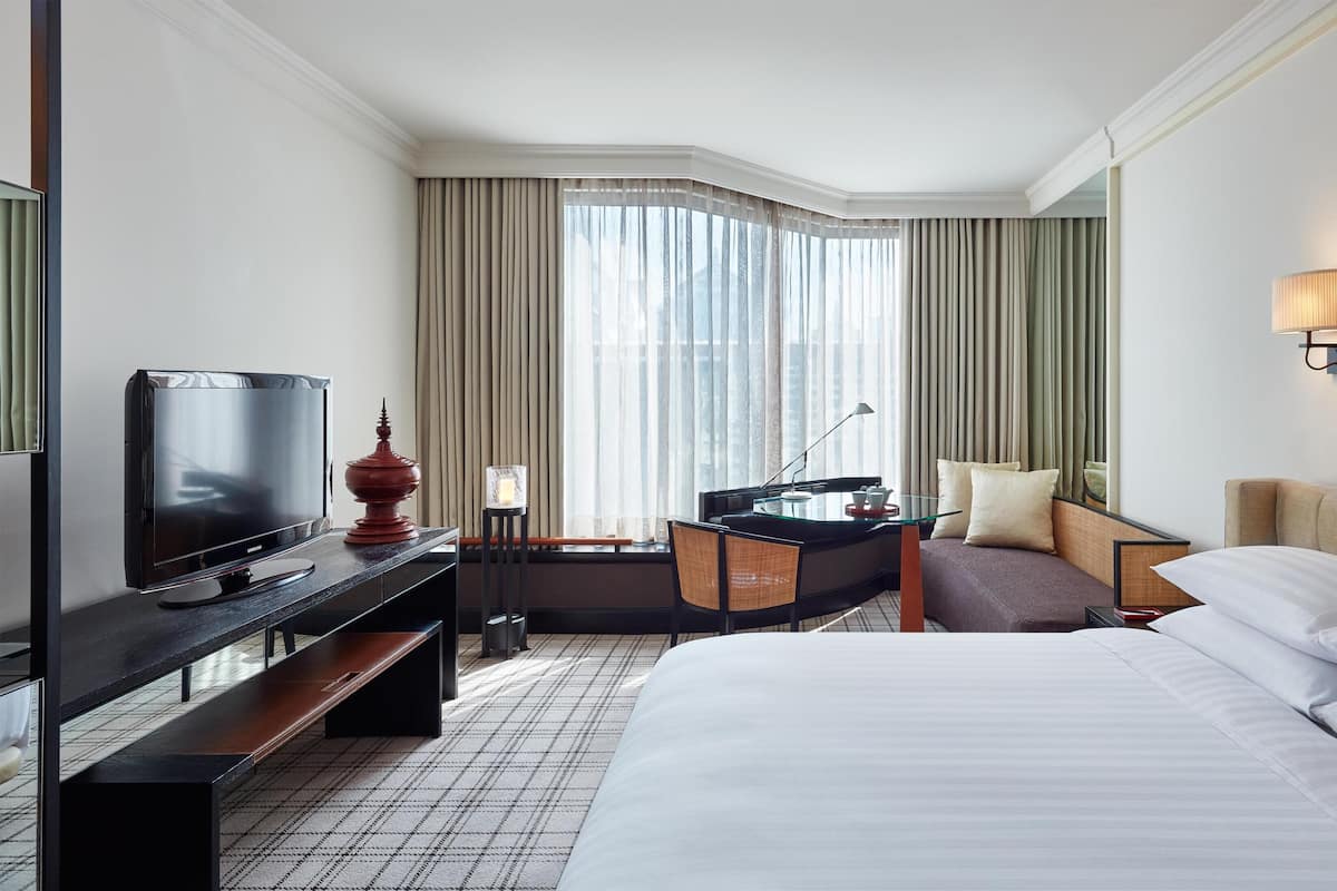 Una habitación de hotel con cama, escritorio con televisor, lámpara y una silla.