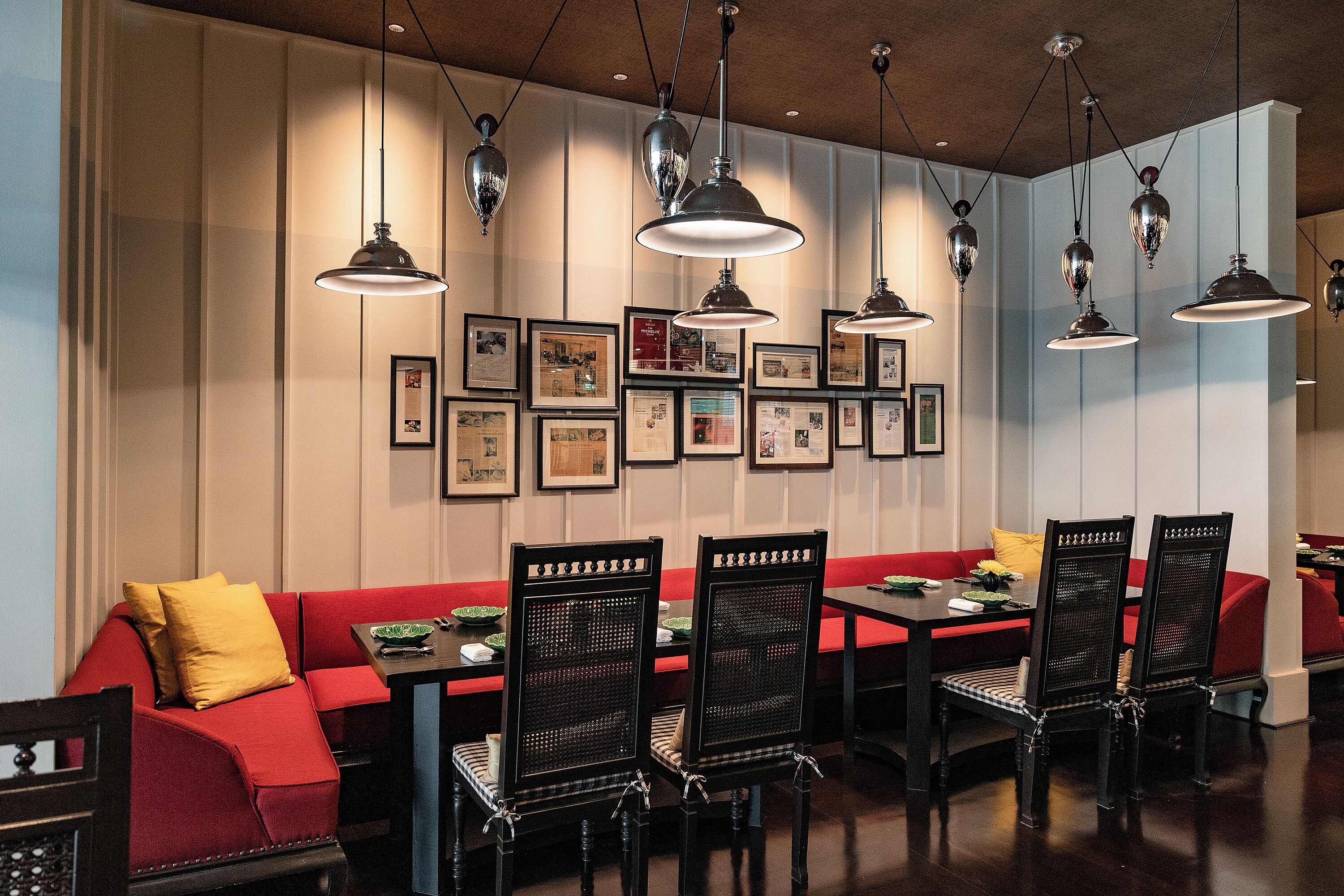A dining area with a red sofa, black chairs, and multiple hanging pendant lights.