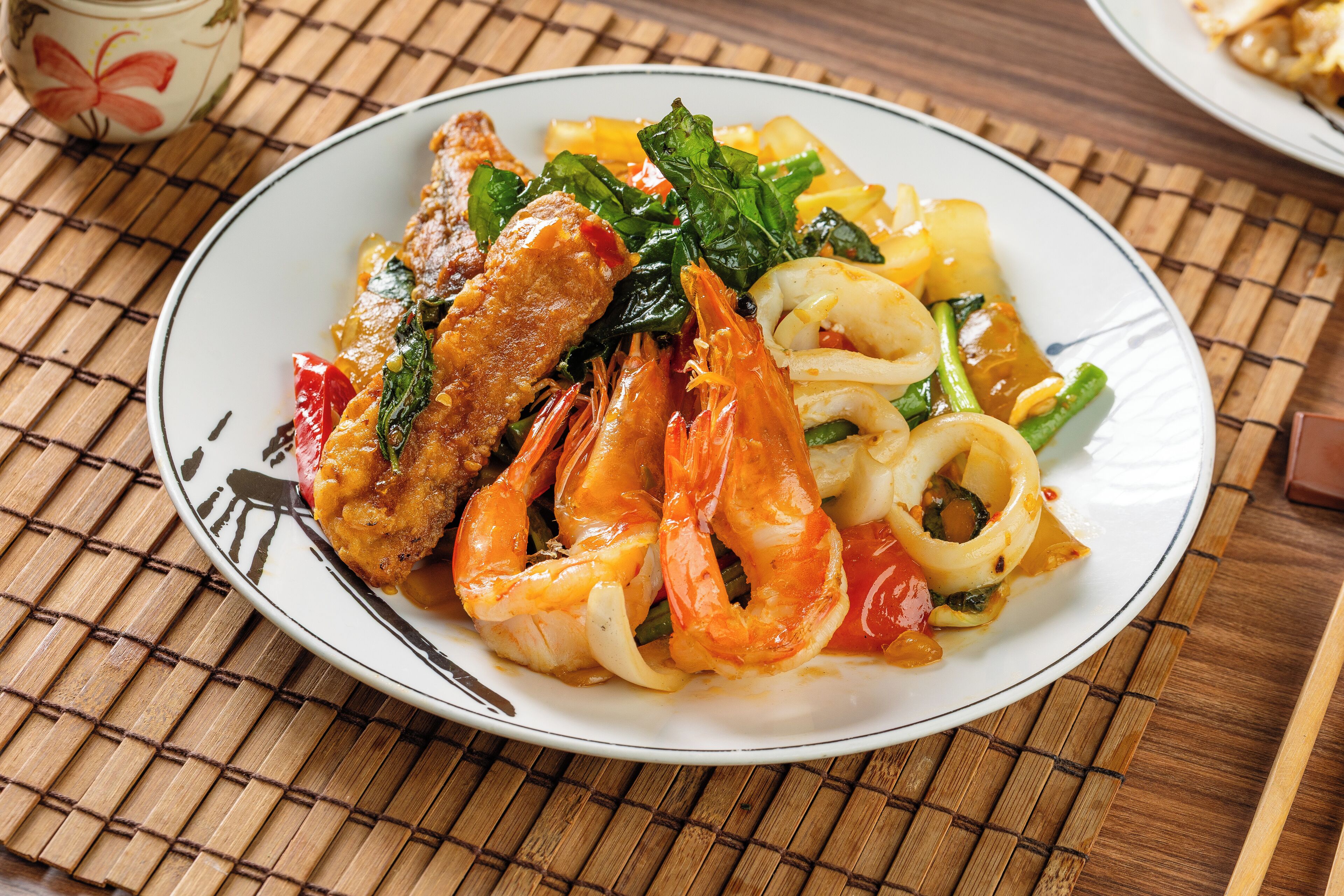 A plate of food with shrimp and vegetables on a bamboo mat.