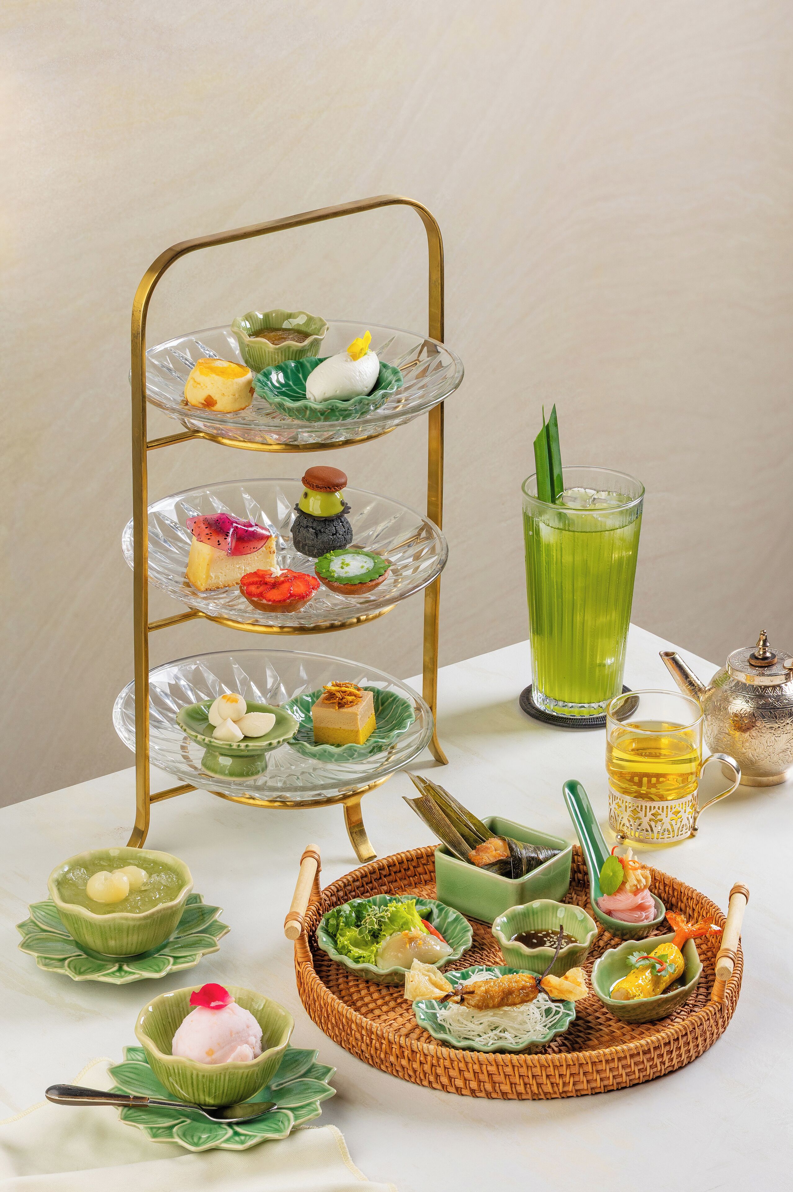 A multi-tiered glass dessert stand with various sweets and a green beverage.