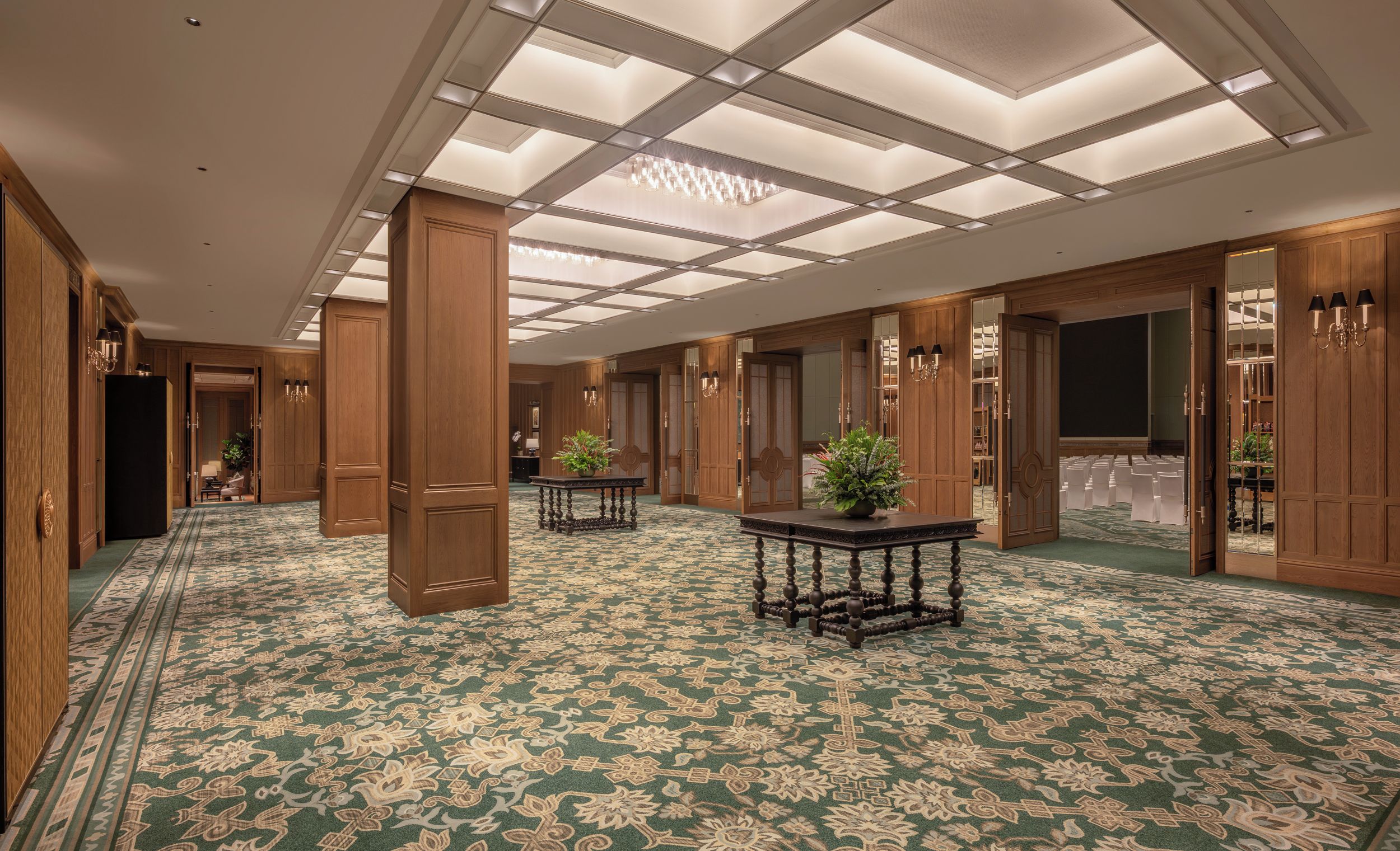 Un couloir d’hôtel avec des boiseries, une moquette à motifs et un lustre.