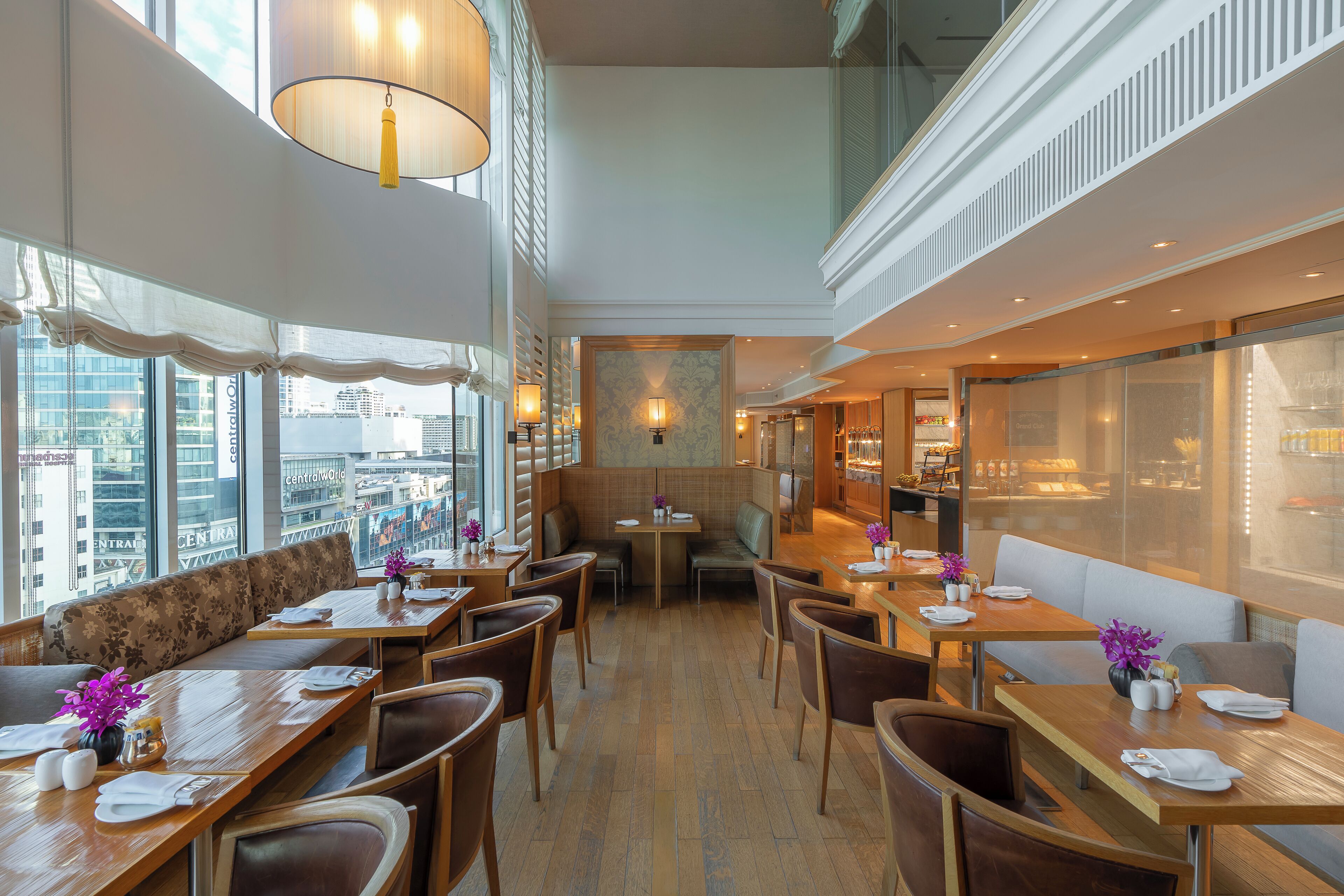 A restaurant with high ceilings, large windows, and a view of the city. Tables are set with white tablecloths and centerpieces.