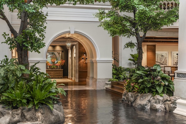 An indoor lobby with a wet floor, a grand archway, and lush greenery.