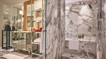 A luxurious bathroom with a marble shower, a glass-enclosed vanity, and a mirror with a decorative frame.