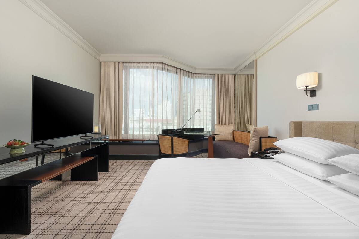 Una habitación de hotel con una cama grande, un televisor de pantalla plana, un escritorio con una silla y una ventana con cortinas.