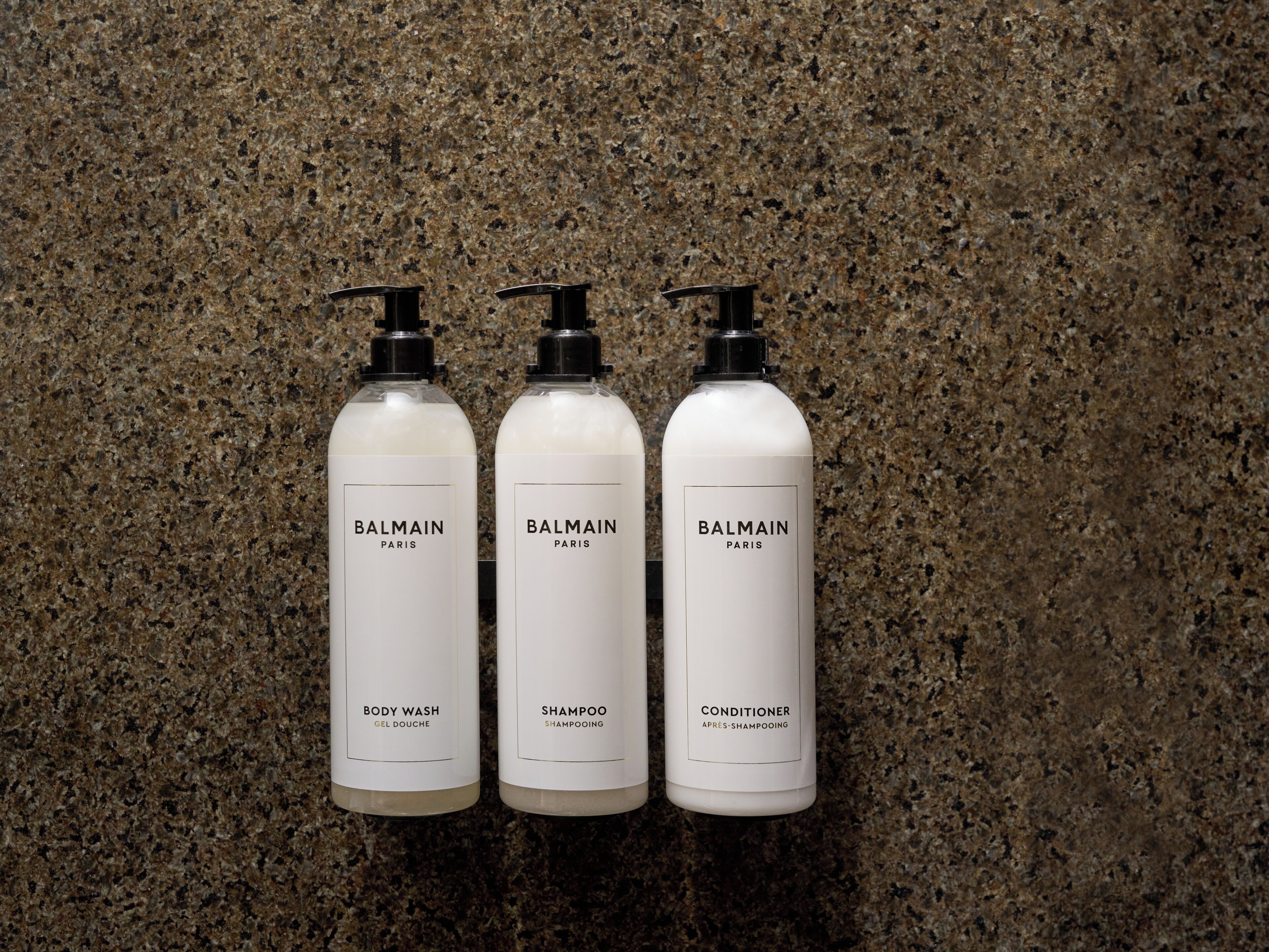 Tre Balmain Paris flasker med shower gel, shampoo og balsam foran en baggrund med plettet granit.
