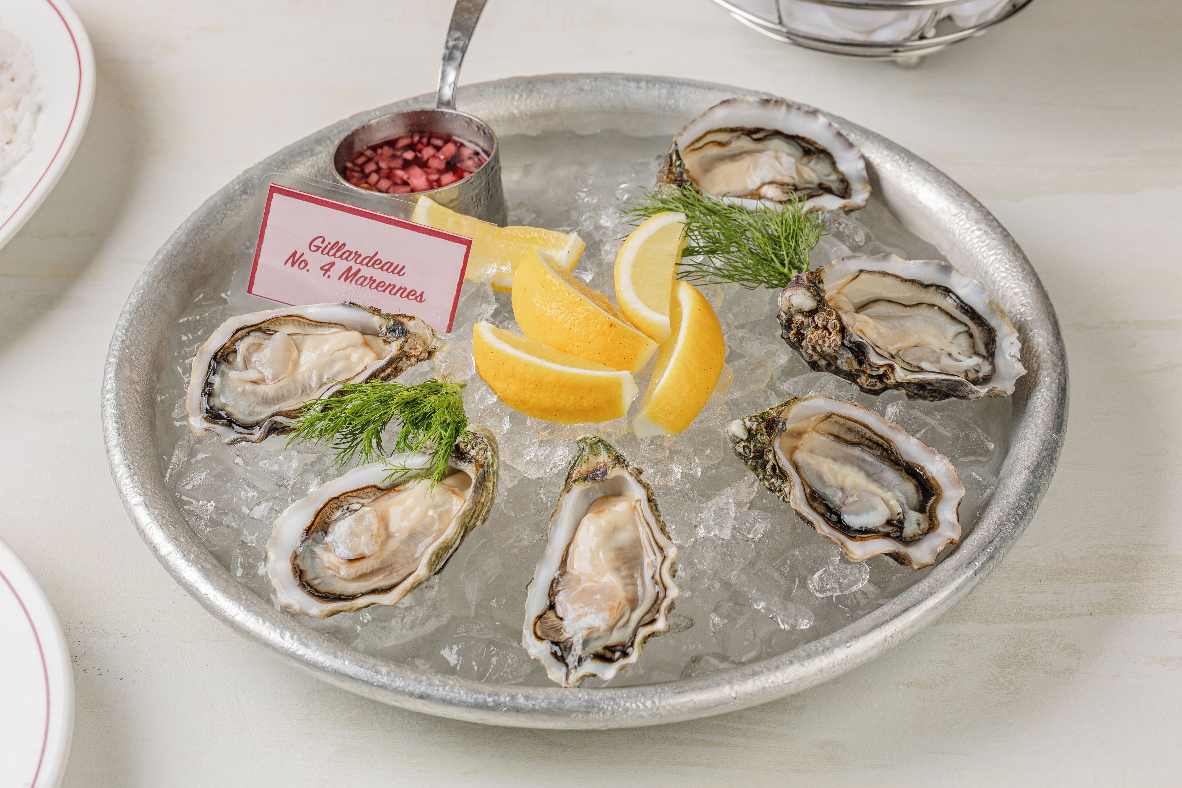 A plate of oysters on ice with lemon wedges and dill garnish.