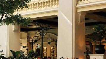 A hotel lobby with a high ceiling, ornate columns, and a seating area with tables and chairs.