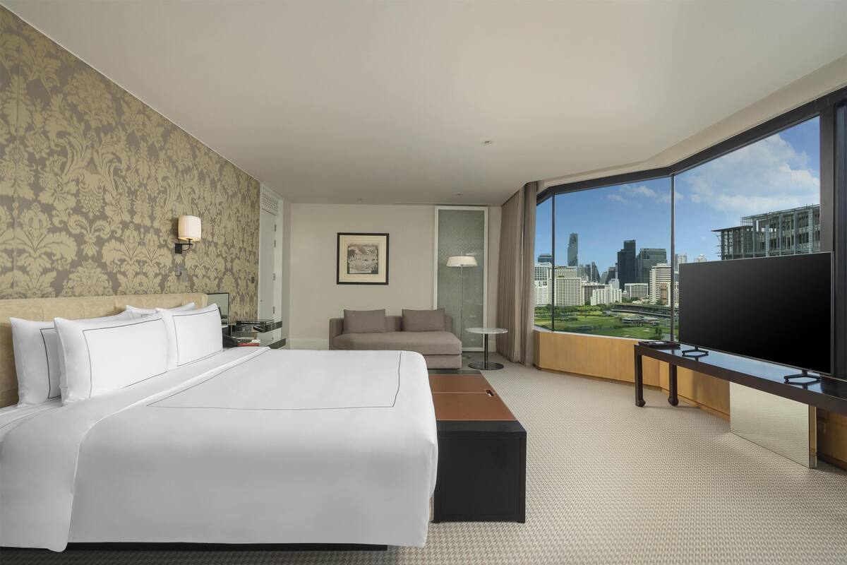 Habitación de hotel con una cama grande, un sofá, un televisor y vistas a la ciudad.