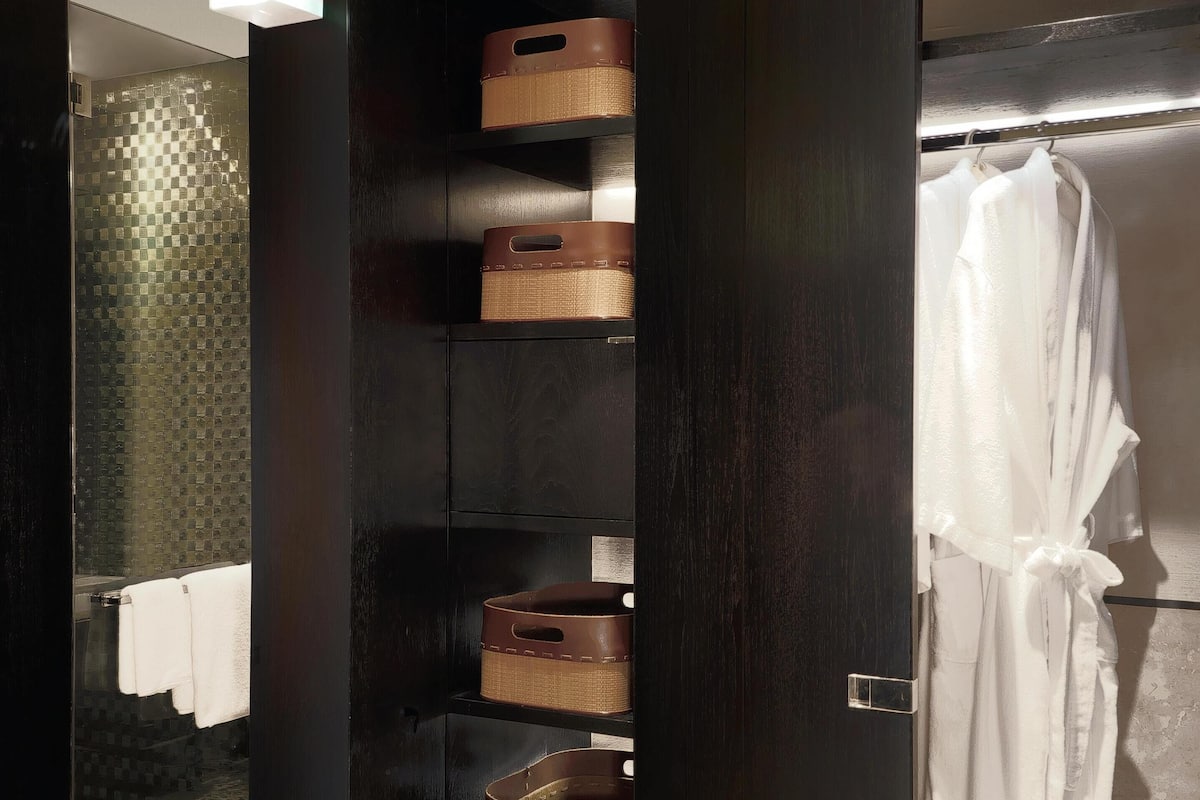 Un baño moderno con tocador de madera oscura, estantes abiertos con cestas, una bata blanca colgada y baldosas de suelo estampadas.