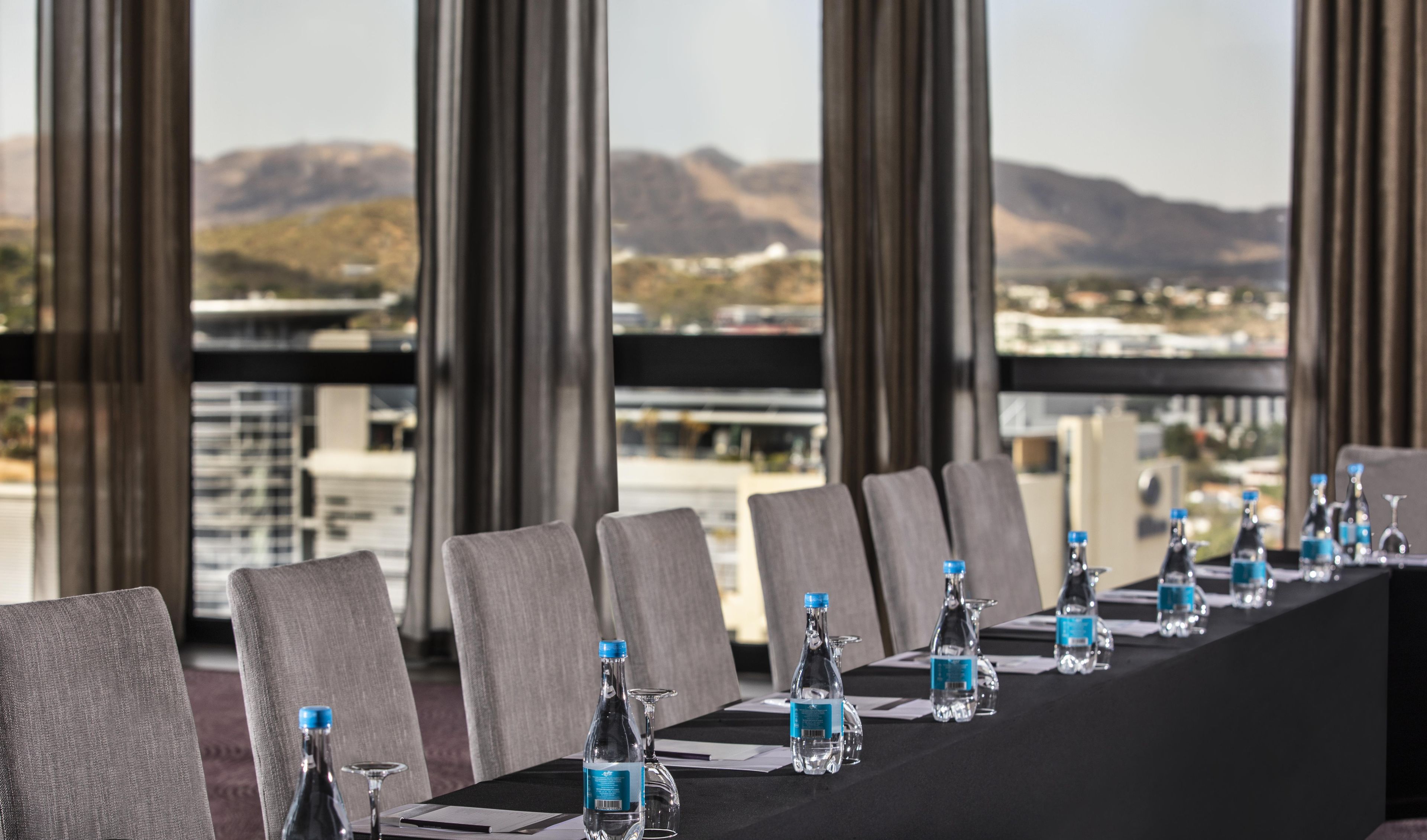 A conference table with chairs, water bottles, and glasses, set against a backdrop of mountains and a cityscape.