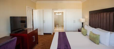 Habitación de hotel con cama, televisor, escritorio y baño visible a través de una puerta abierta.