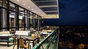 Terraza en la azotea con mobiliario exterior, ventanas amplias y vistas a la ciudad de noche.