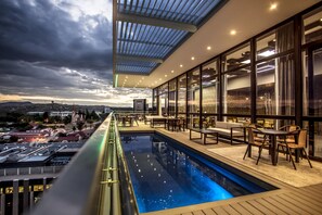 Piscina infinita con vistas al paisaje urbano, zona de estar al aire libre y un porche cubierto.