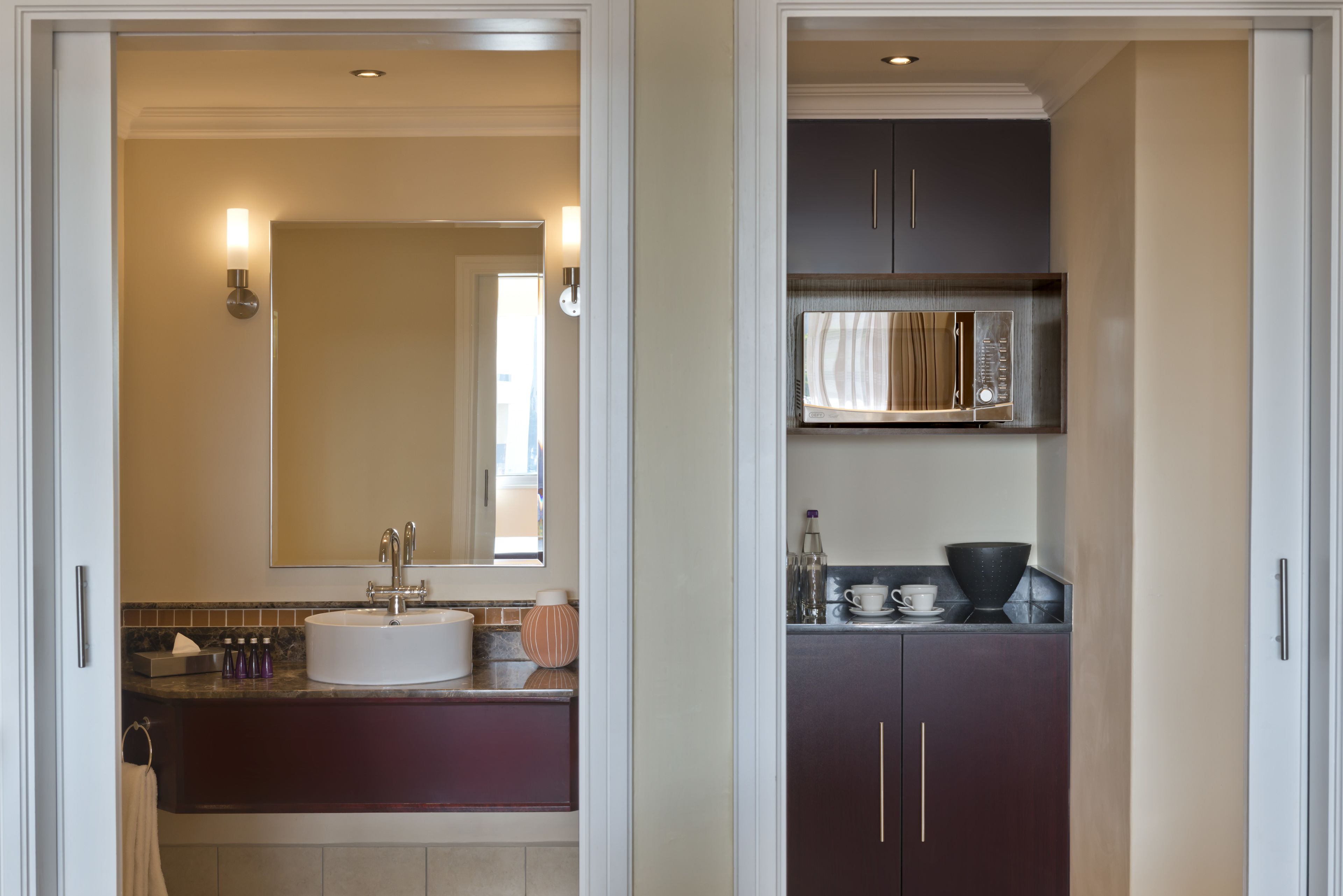 Un baño moderno con lavamanos blanco, espejo y muebles de almacenamiento oscuros.