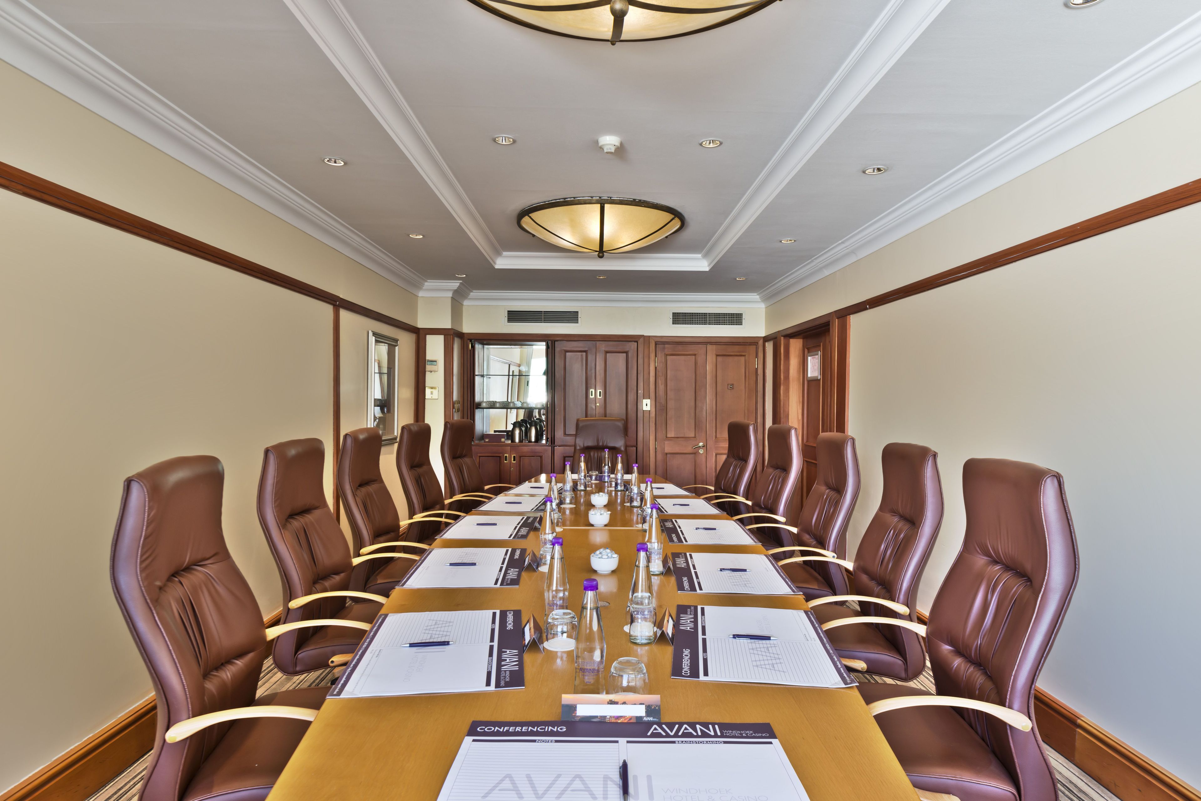 A conference room with a long table, brown leather chairs, and a chandelier.