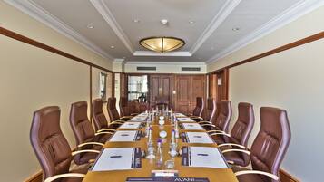A conference room with a long table, brown leather chairs, and a chandelier.
