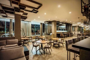 A modern restaurant with a mix of seating options including tables and sofas, large windows offering views of the city, and a contemporary interior design. - Avani Windhoek Hotel & Casino (Windhoek)
