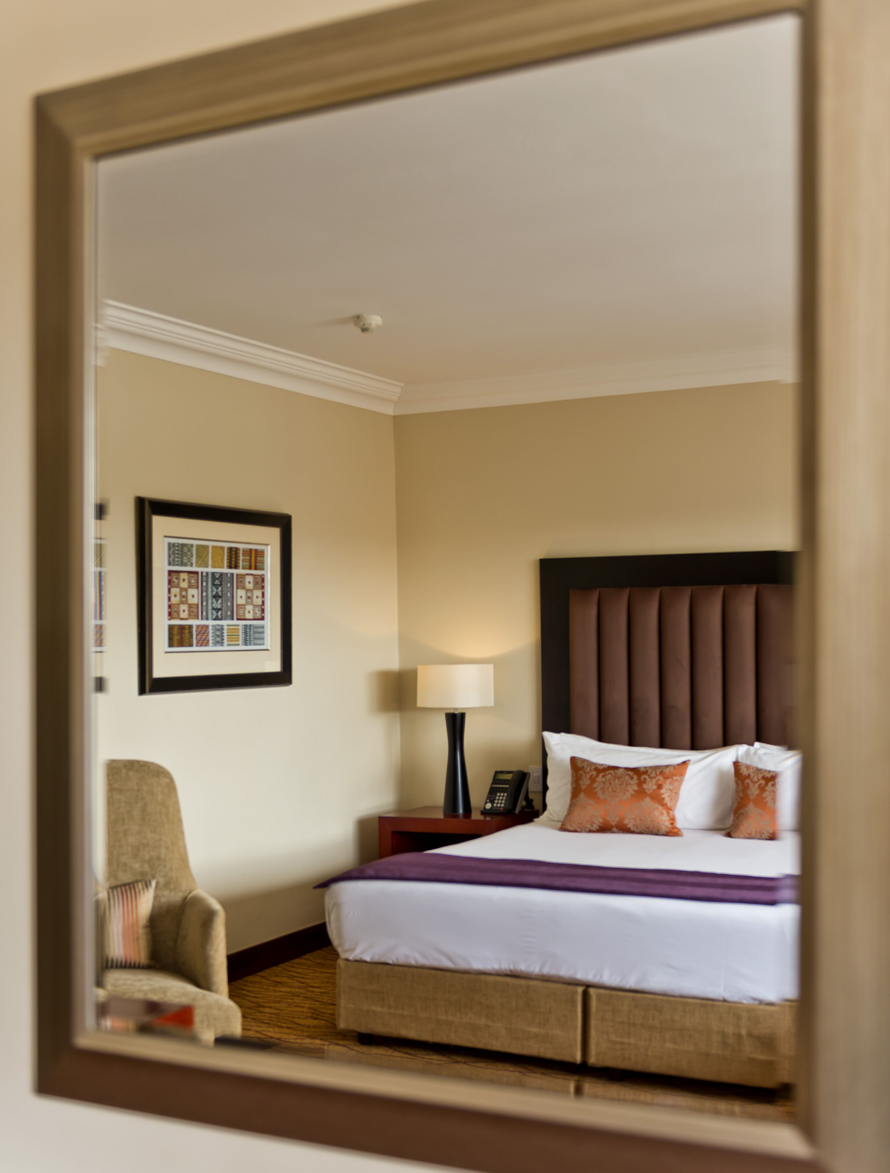 Ein Hotelzimmer mit einem Bett, einem Nachttisch, einer Lampe, einem Sessel und einem gerahmten Bild an der Wand.
