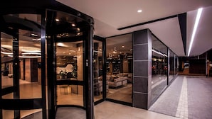 Un moderno vestíbulo de hotel con puerta giratoria, zona de estar con sofás e interior bien iluminado.