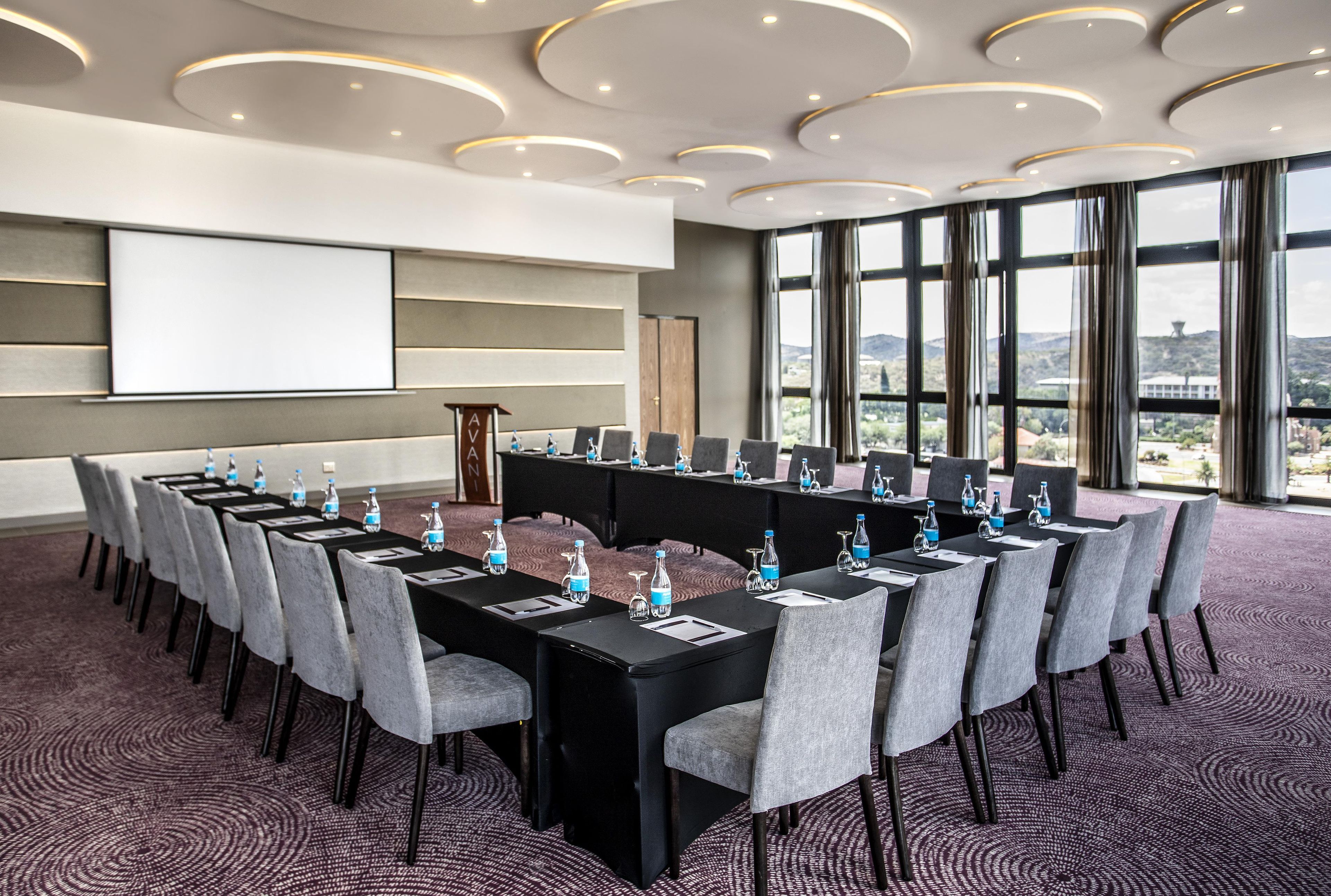 A conference room with a long table, chairs, water bottles, and a projector screen.