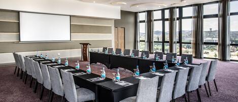 A conference room with a long table, chairs, water bottles, and a projector screen.