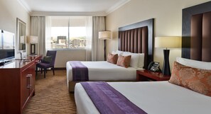 A hotel room with two beds, a desk with a TV, a chair, and a view of the city. - Avani Windhoek Hotel & Casino (Windhoek)