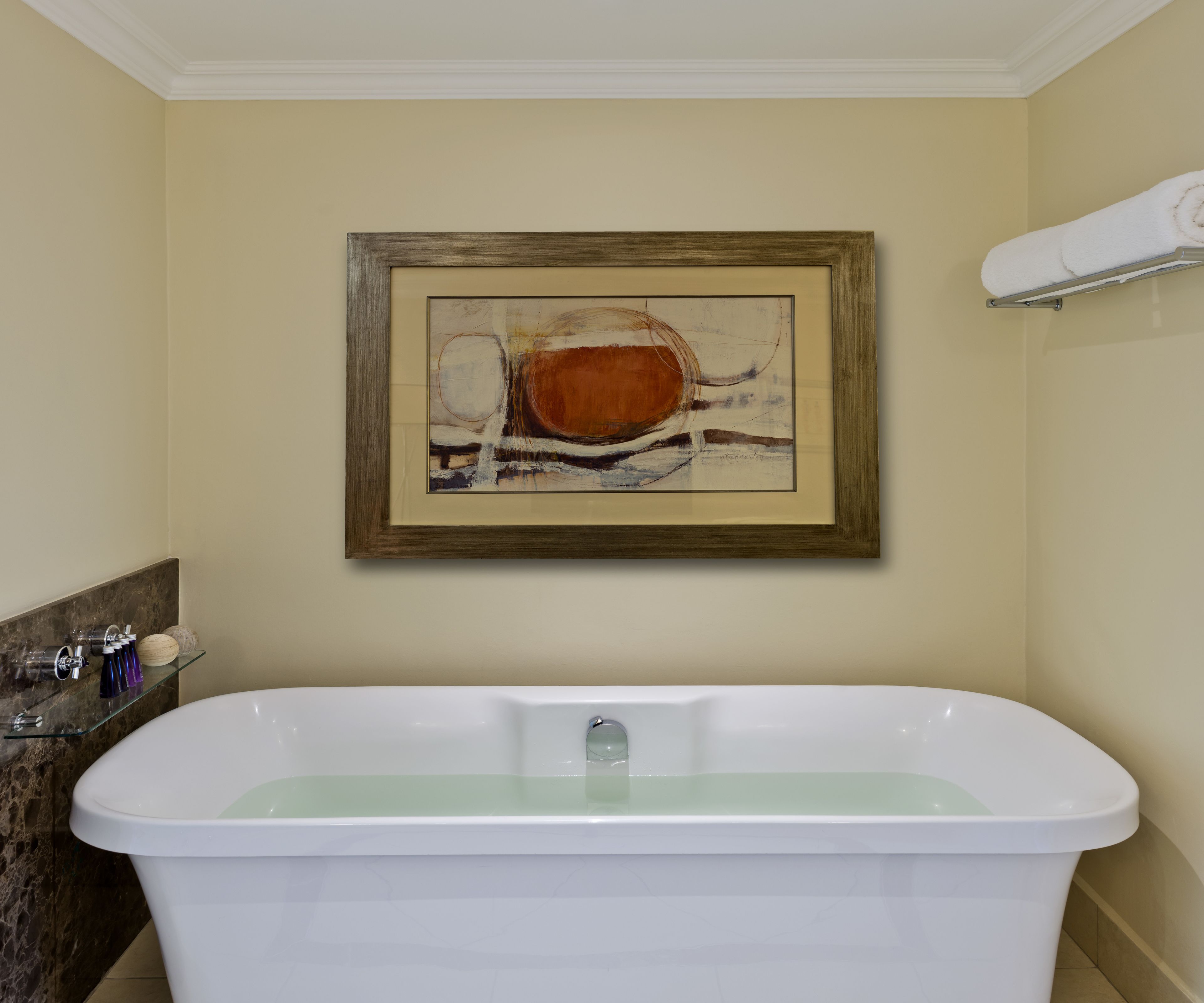 Une salle de bain avec une baignoire blanche, un tableau abstrait encadré accroché au mur et un porte-serviettes au-dessus de la baignoire.