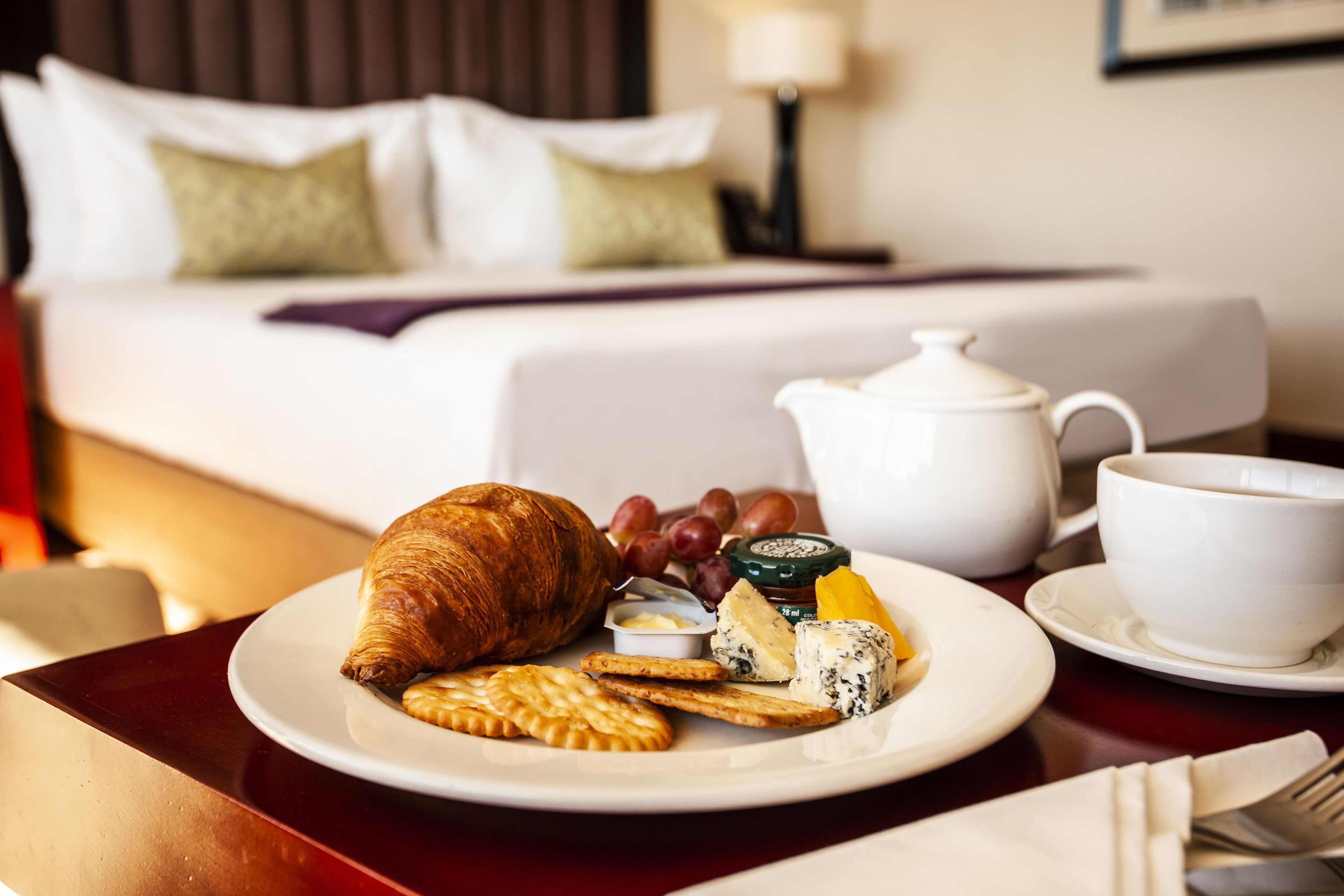 A breakfast setting with a croissant, cheese, crackers, and a teapot on a table.
