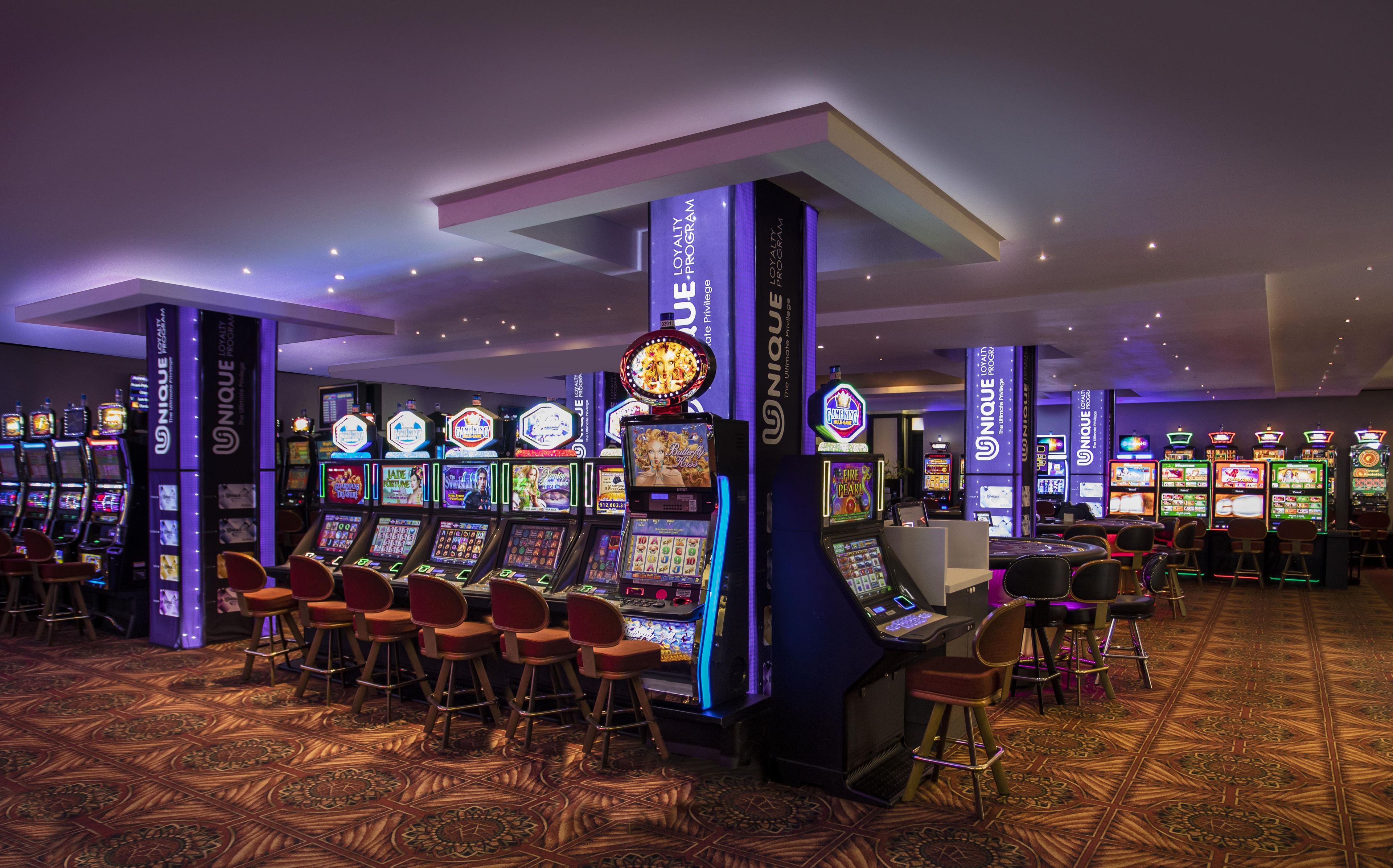 A casino floor with multiple slot machines, bar stools, and a patterned carpet.