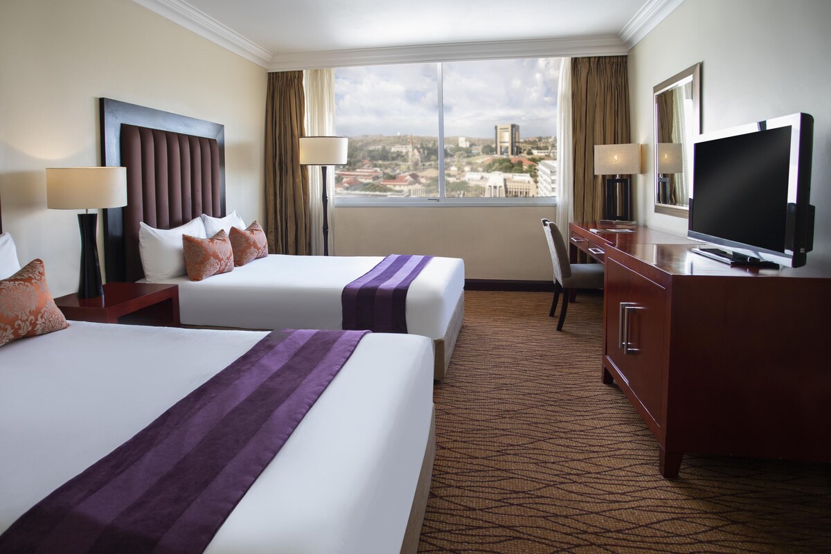 Habitación de hotel con dos camas, un televisor, un escritorio y vistas a la ciudad.