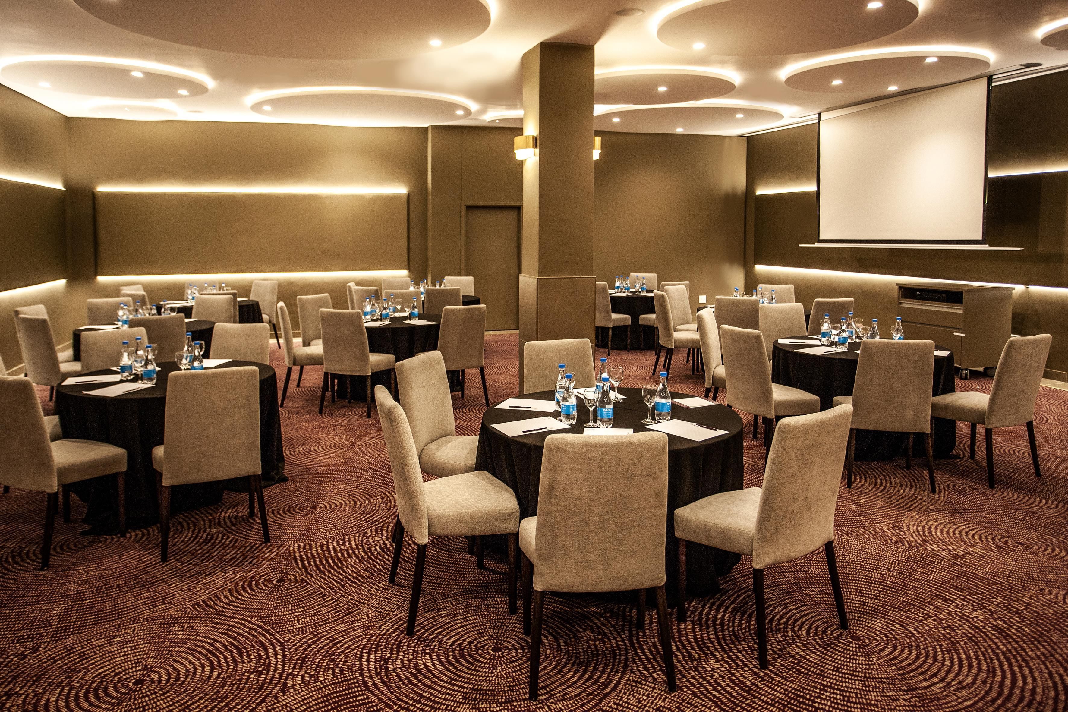 A conference room with multiple tables, chairs, and a projector screen.