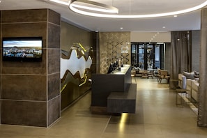 A modern hotel lobby with a reception desk, seating area, and a large TV screen displaying a cityscape. - Avani Windhoek Hotel & Casino (Windhoek)