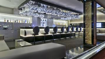 Un espace bar moderne doté d’un long comptoir, de nombreux tabourets et d’un plafond décoratif agrémenté de luminaires suspendus.