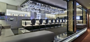 A modern bar area with a long counter, multiple bar stools, and a decorative ceiling with hanging lights. - Avani Windhoek Hotel & Casino (Windhoek)