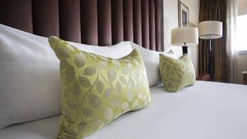 Una habitación de hotel con una cama grande, dos almohadas con estampado de hojas, un cabecero, una lámpara y un cuadro en la pared.