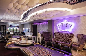 A casino interior with a roulette table, gaming machines, and plush seating.