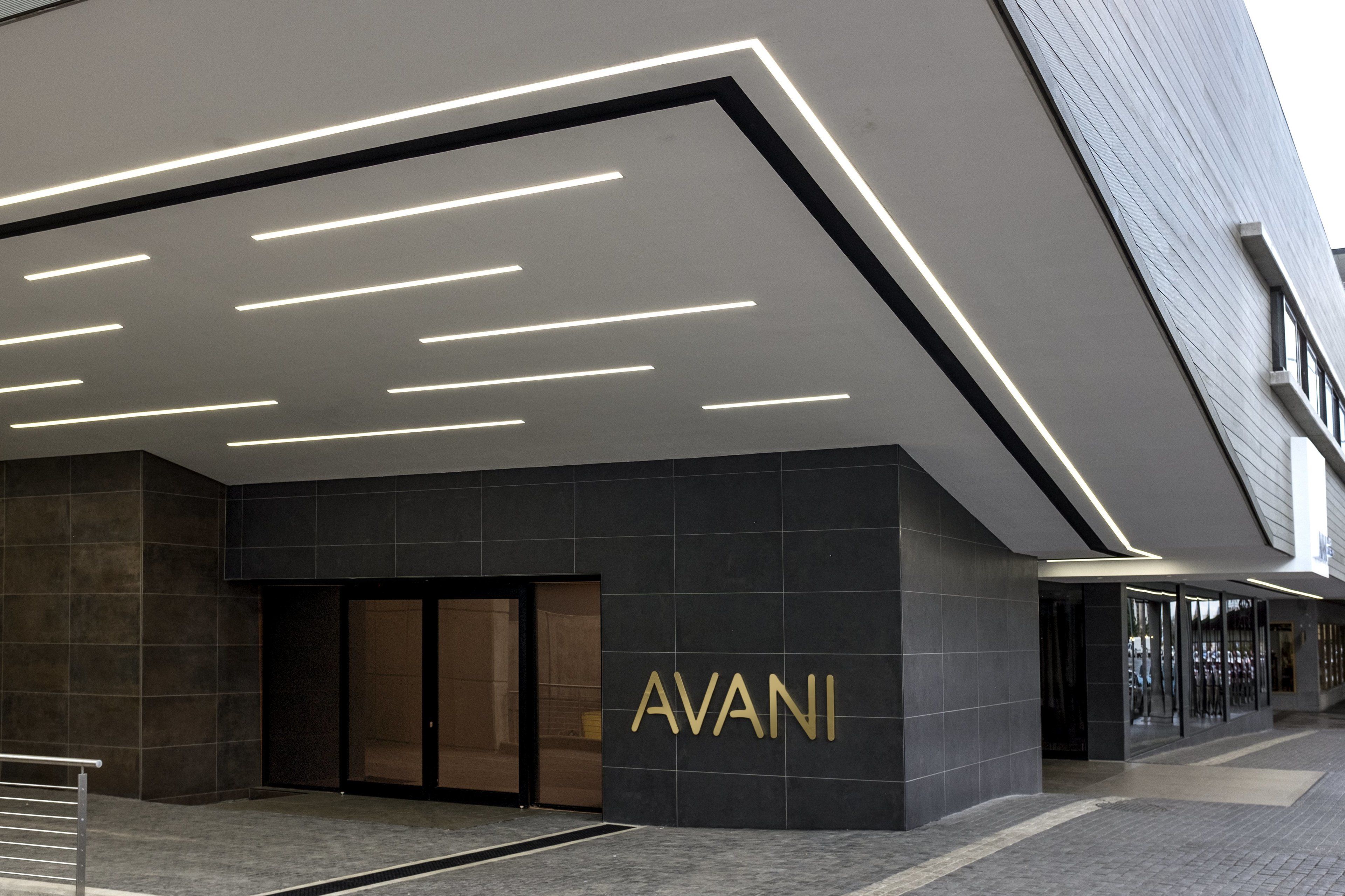 Une entrée moderne, marquée par une enseigne « AVANI » bien visible, un éclairage élégant et un style architectural épuré et contemporain.