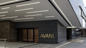 Una entrada moderna de edificio con un llamativo letrero 'AVANI', un diseño de iluminación elegante y un estilo arquitectónico contemporáneo y limpio.