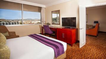 A hotel room with a large bed, a desk with a TV, and a view of the city.