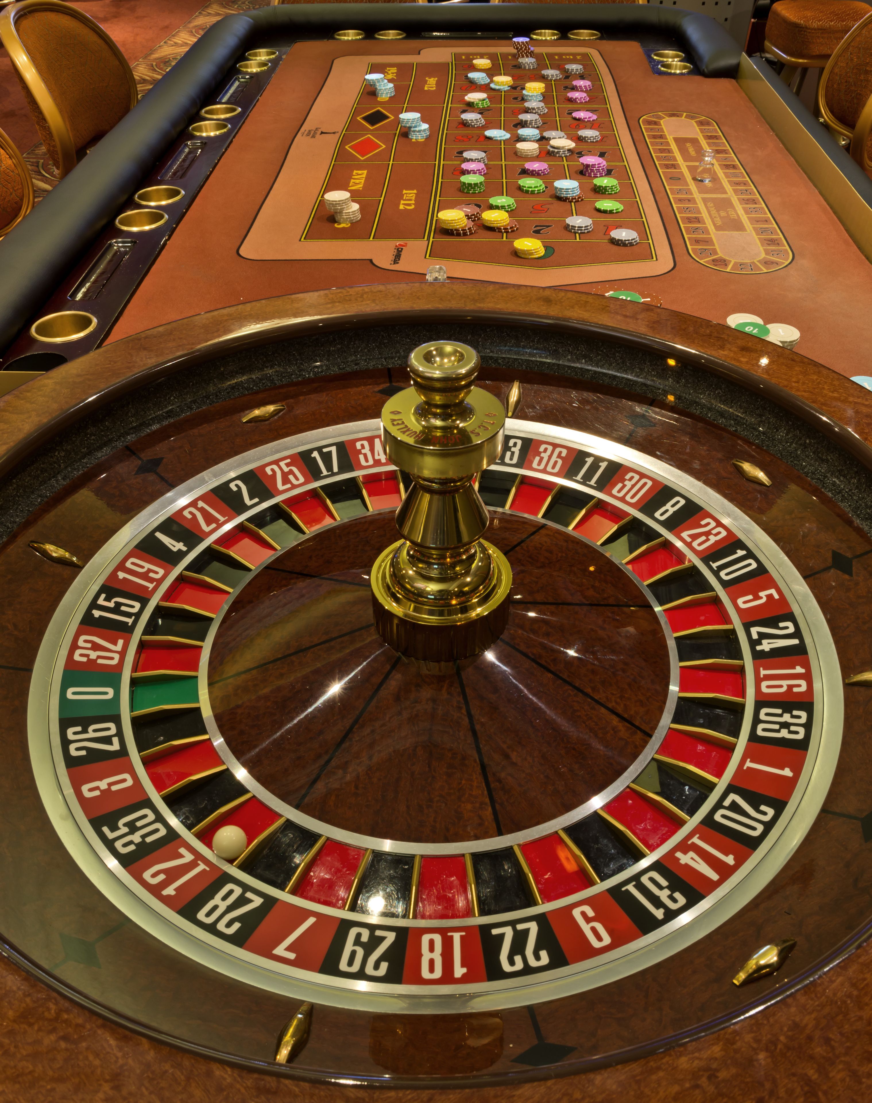 A roulette wheel and betting table with chips and a dealer's hand.