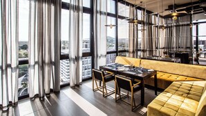 Un comedor moderno con una mesa para dos, un sofá amarillo y grandes ventanales con vista a la ciudad.