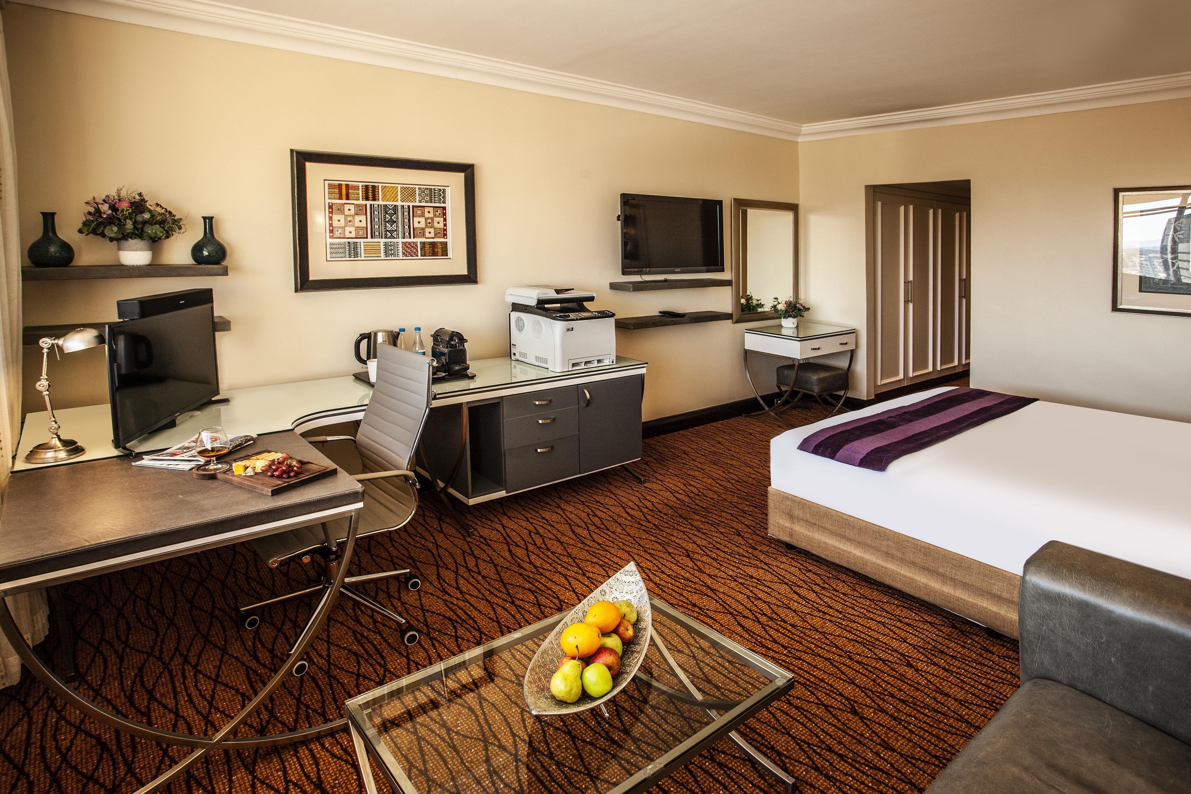 Habitación de hotel con cama, escritorio, silla, televisor y un cuadro en la pared.