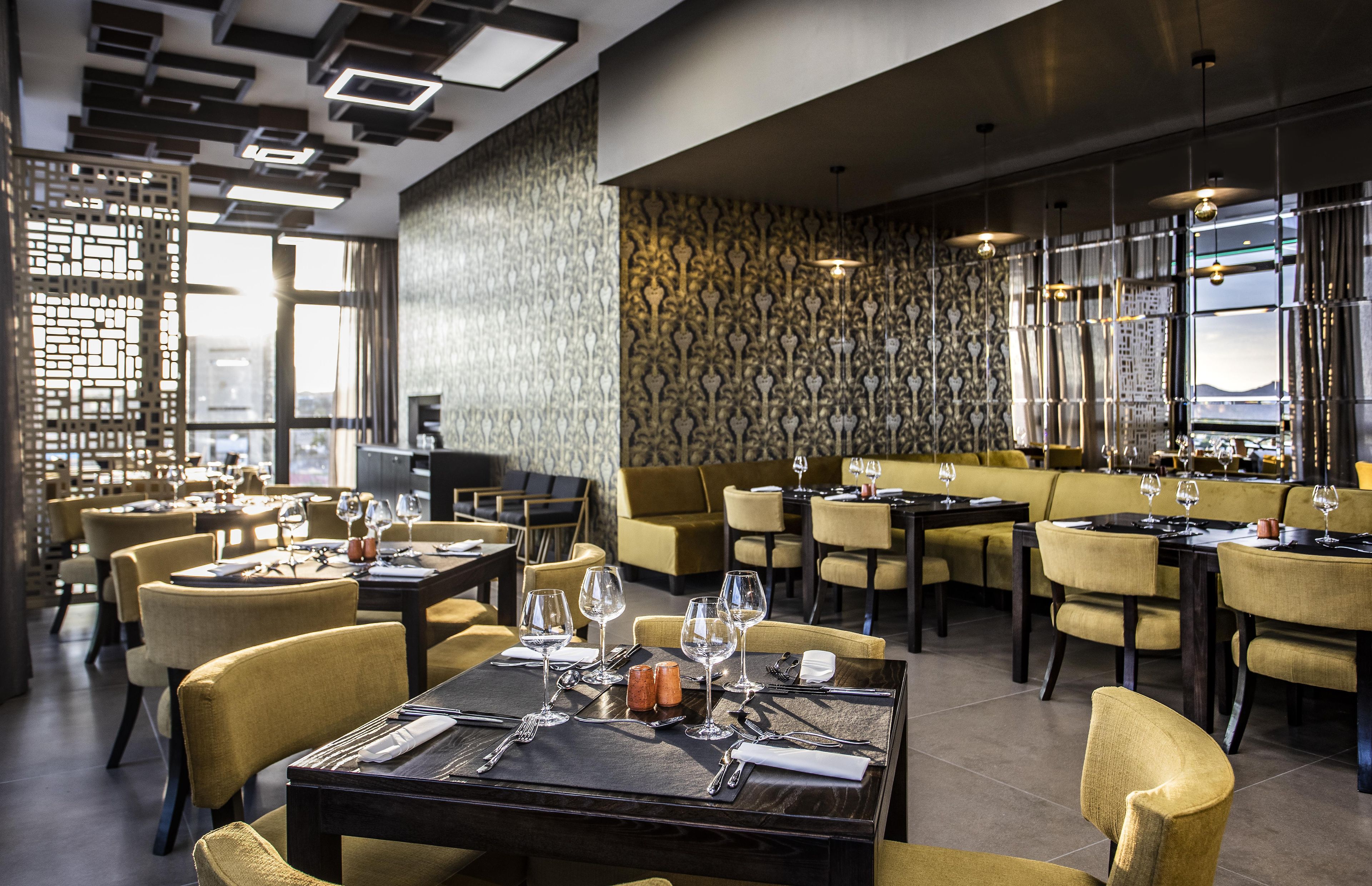 L’intérieur d’un restaurant, avec plusieurs tables, des chaises et un mur orné de motifs.