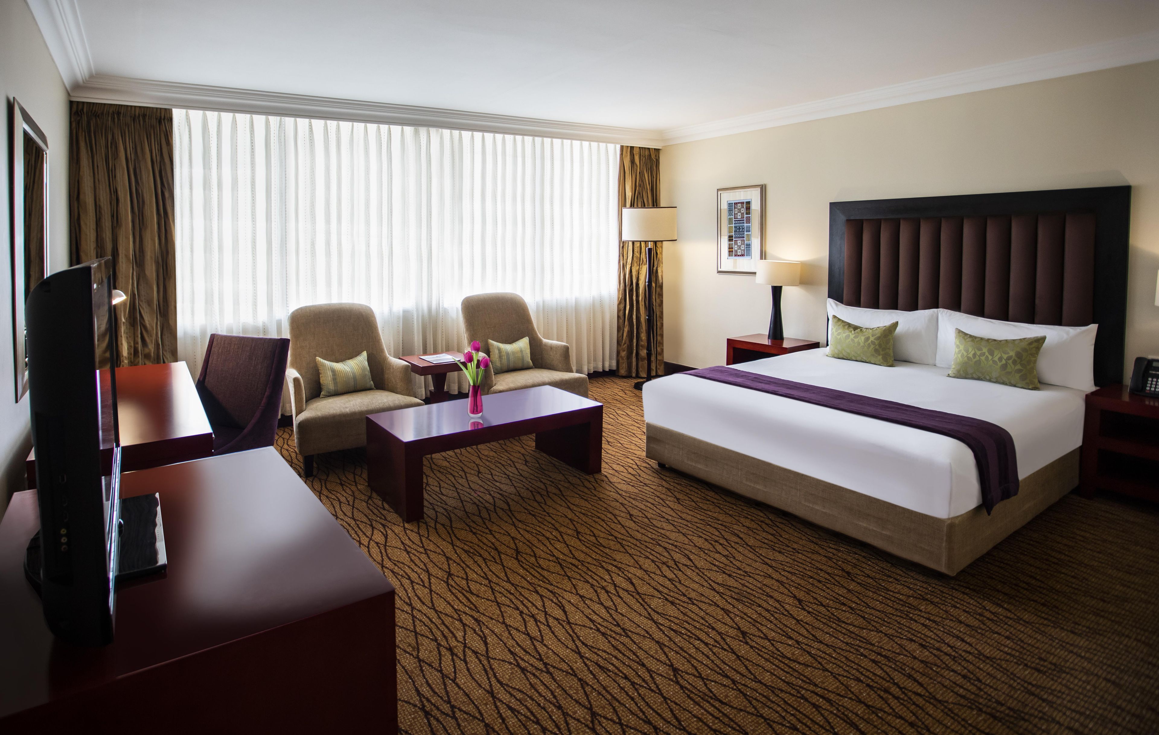 A hotel room with a large bed, two armchairs, a coffee table, a TV, and a desk.